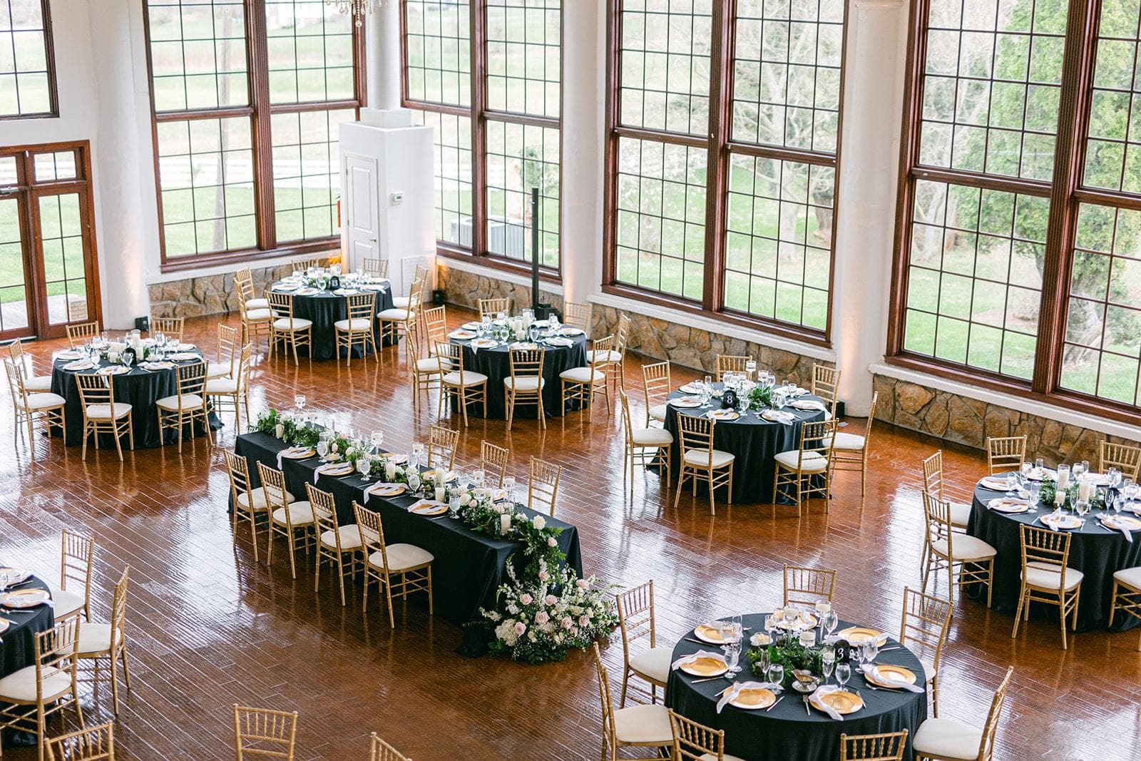 Corporate gala rounds in forest-green linens beneath tall windows and a crystal chandelier
